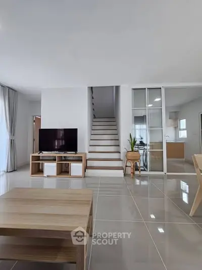 Modern living room with sleek staircase and open kitchen layout, featuring stylish furniture and natural light.