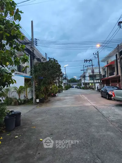 Charming residential street view with lush greenery and modern townhouses under a serene sky.