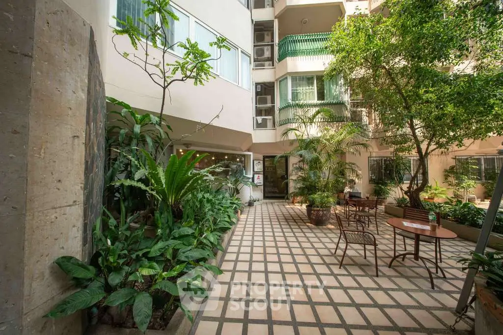 Charming garden courtyard with lush greenery and cozy seating area in modern building.