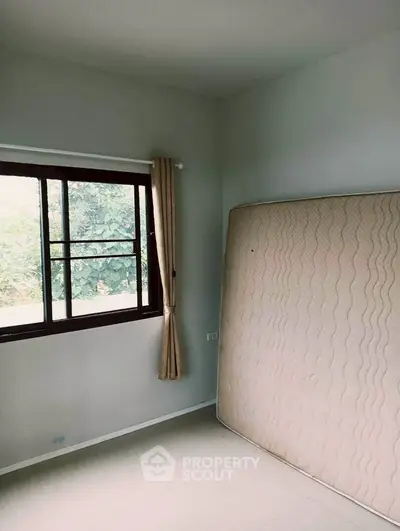 Spacious bedroom with large window and natural light, featuring a mattress against the wall.