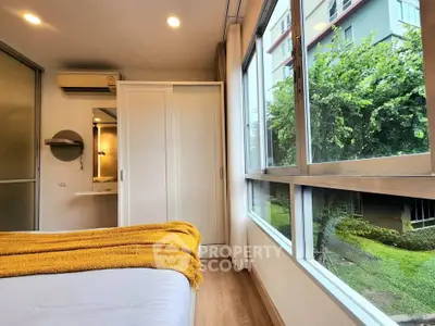 Bright bedroom with large windows offering lush garden views, featuring modern decor and ample natural light.