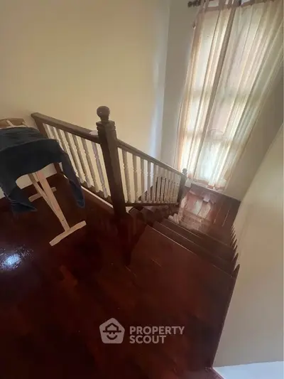 Elegant wooden staircase with natural light from tall window, perfect for a cozy home ambiance.