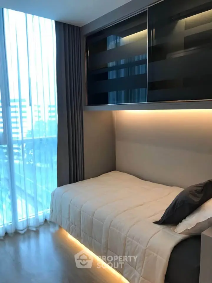 Modern bedroom with sleek design and ambient lighting, featuring large windows and stylish storage solutions.