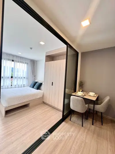 Modern studio apartment with cozy bedroom and dining area, featuring sleek sliding glass doors and elegant decor.