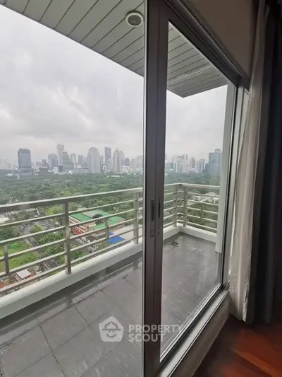 Stunning cityscape view from a high-rise balcony with glass doors and lush greenery.