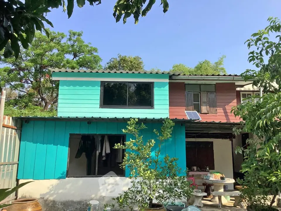 Charming two-story house with vibrant teal exterior and lush greenery, perfect for nature lovers.