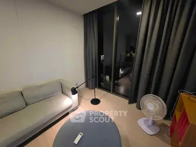 Modern living room with cozy sofa, floor lamp, and fan, featuring large window with elegant curtains.