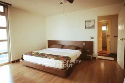 Spacious bedroom with wooden flooring and modern decor in a bright apartment.