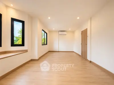 Spacious empty room with wooden flooring and large windows offering natural light.