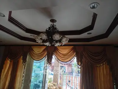 Elegant living room with ornate chandelier and luxurious drapes, offering a glimpse of the outdoor garden.