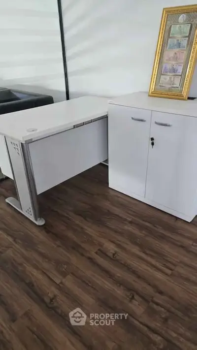 Modern office space with sleek white desk and cabinet on elegant wooden flooring.