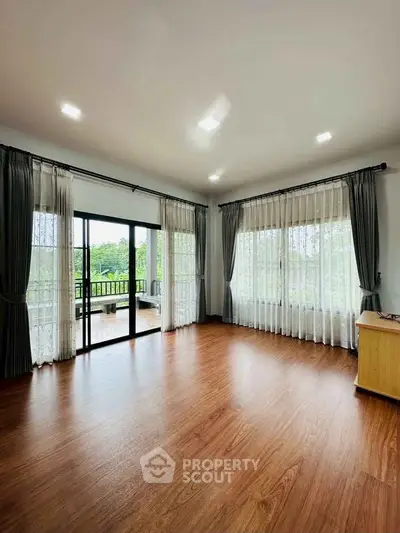 Spacious living room with large windows and balcony access, featuring elegant curtains and wooden flooring.