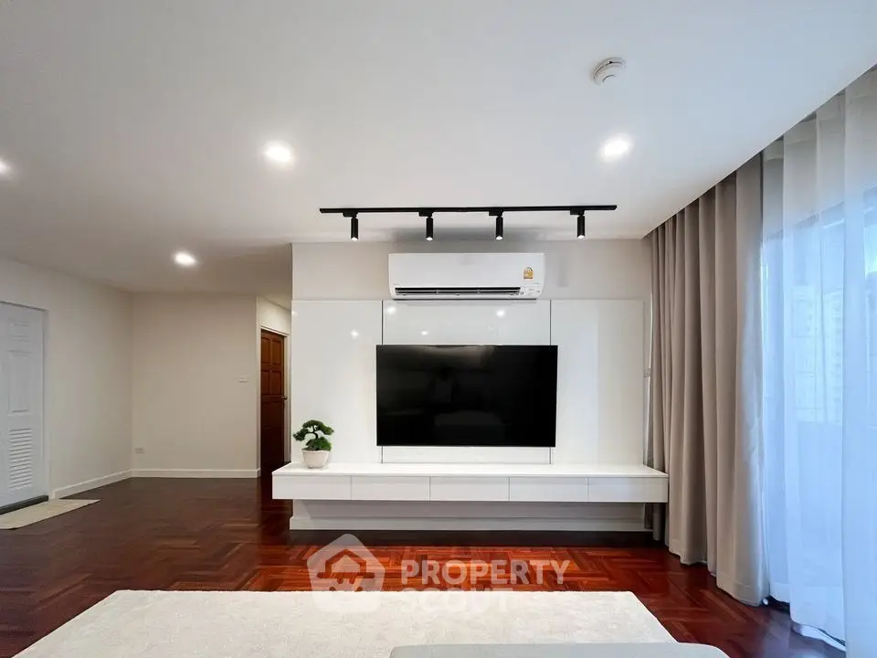 Spacious modern living room with sleek TV setup and elegant hardwood flooring.