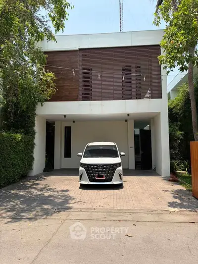 Modern two-story house with sleek design and spacious driveway in a lush green setting.