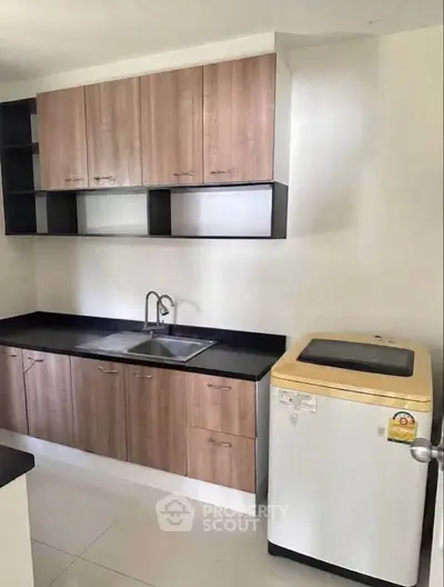 Modern kitchen with wooden cabinets and washing machine in sleek apartment.