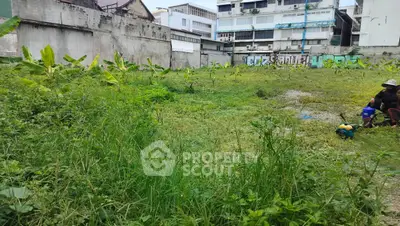Vacant urban lot with overgrown grass and surrounding buildings, ideal for development opportunities.