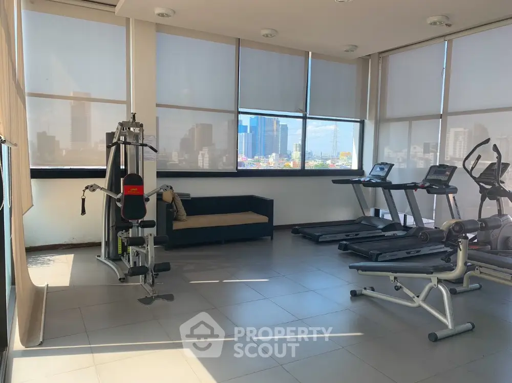 Modern gym with city view, featuring exercise equipment and natural light.