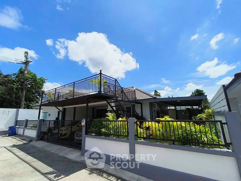 Charming single-story home with rooftop terrace and lush garden under a bright blue sky.