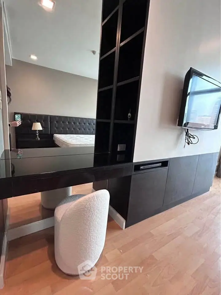 Modern bedroom with sleek black shelving and mounted TV, featuring a cozy white chair and hardwood floors.