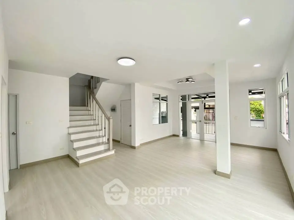Spacious modern living room with elegant staircase and large windows for natural light.