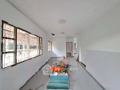 Spacious interior under renovation with large windows and construction materials.