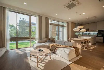 Luxurious open-plan living room with modern kitchen and garden view, featuring elegant decor and ample natural light.