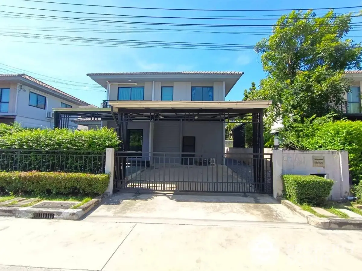 Modern two-story house with gated driveway and lush greenery in suburban neighborhood.