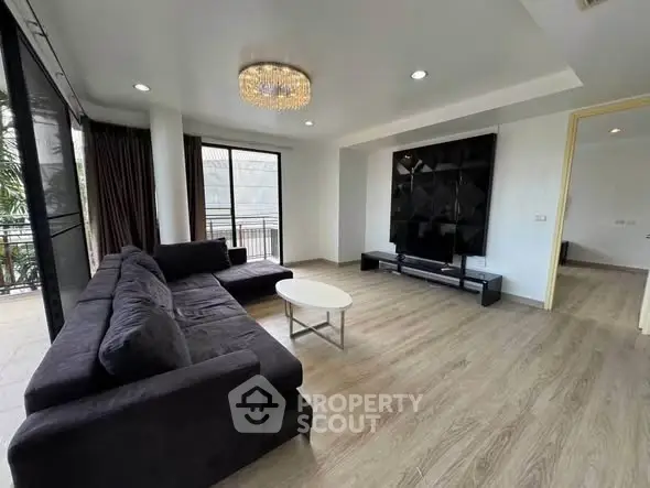 Spacious modern living room with elegant chandelier and large windows opening to a balcony.