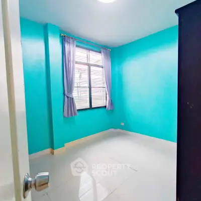 Bright empty bedroom with turquoise walls and large window, ready for personalization.