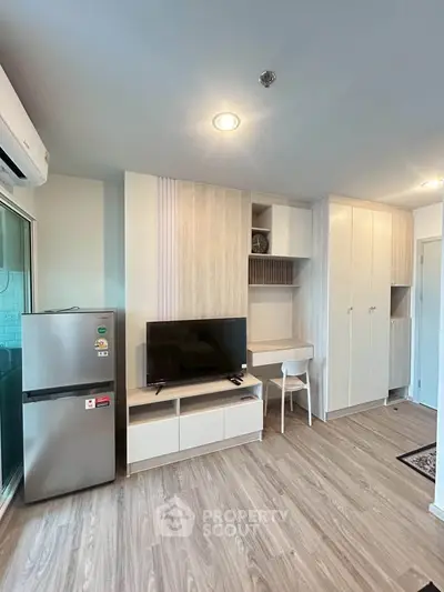 Modern living room with sleek furniture and built-in storage, featuring a TV and refrigerator.