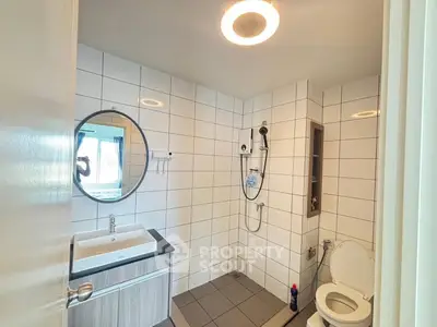 Modern bathroom with sleek fixtures and tiled walls, featuring a round mirror and open shower design.