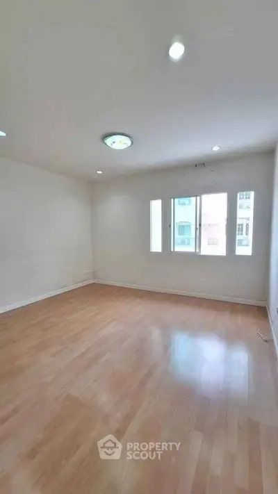 Spacious empty room with wooden flooring and large windows, perfect for customization.