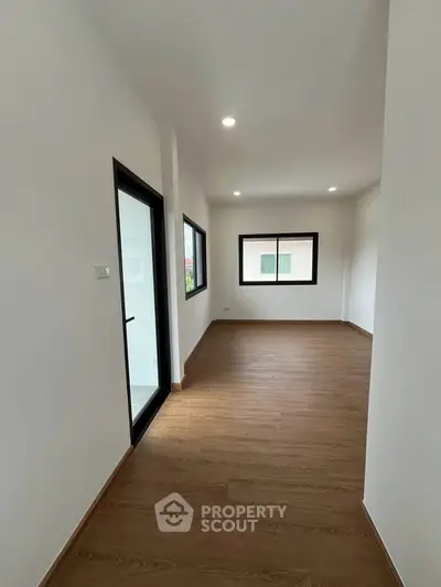 Spacious empty room with wooden flooring and large windows, perfect for customization.