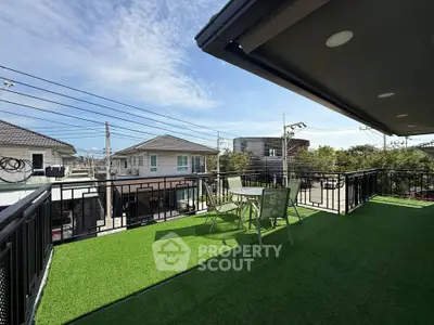 Spacious balcony with artificial grass and outdoor seating, offering a serene neighborhood view.