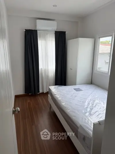 Cozy bedroom with wooden flooring, large window, and air conditioning unit.