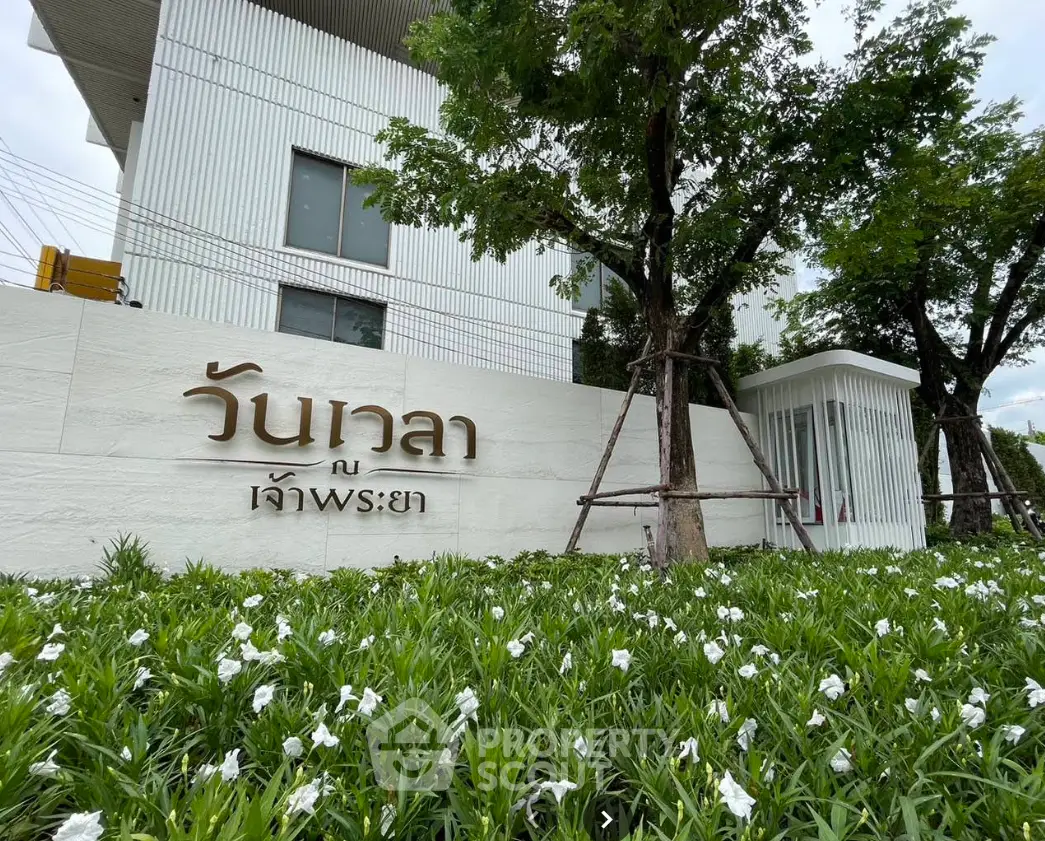 Modern building entrance with lush greenery and stylish signage in a serene setting.