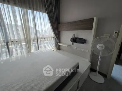 Modern bedroom with large window and city view, featuring a wall-mounted TV bracket and sleek fan.