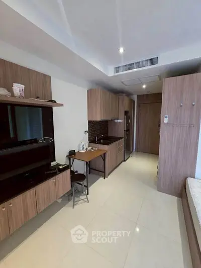 Modern studio apartment with compact kitchen and sleek wooden cabinetry.