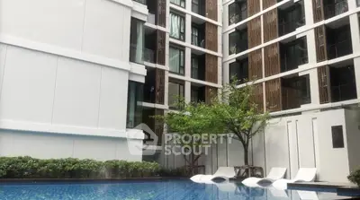 Modern apartment building with poolside relaxation area and lush greenery.
