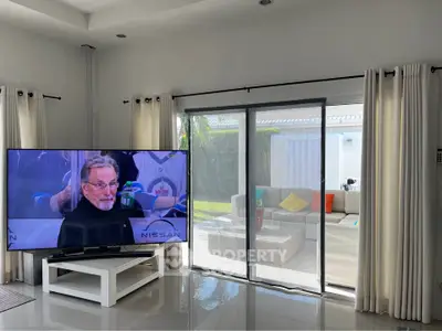 Spacious living room with large TV and sliding glass doors leading to a cozy patio.