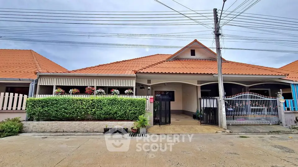 Charming single-story house with red-tiled roof and lush greenery in a serene neighborhood.