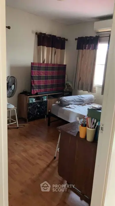 Cozy bedroom with wooden flooring, single bed, and natural light from window.