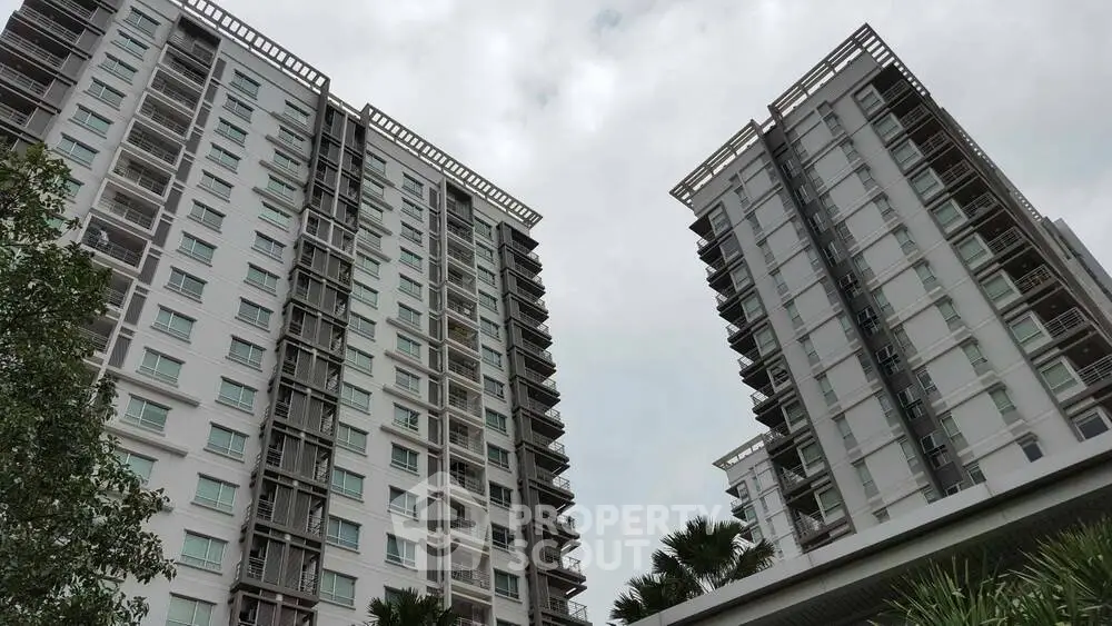 Modern high-rise residential buildings with lush greenery and cloudy sky.