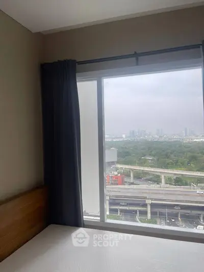 Cozy bedroom with large window offering stunning city and greenery views, perfect for urban living.