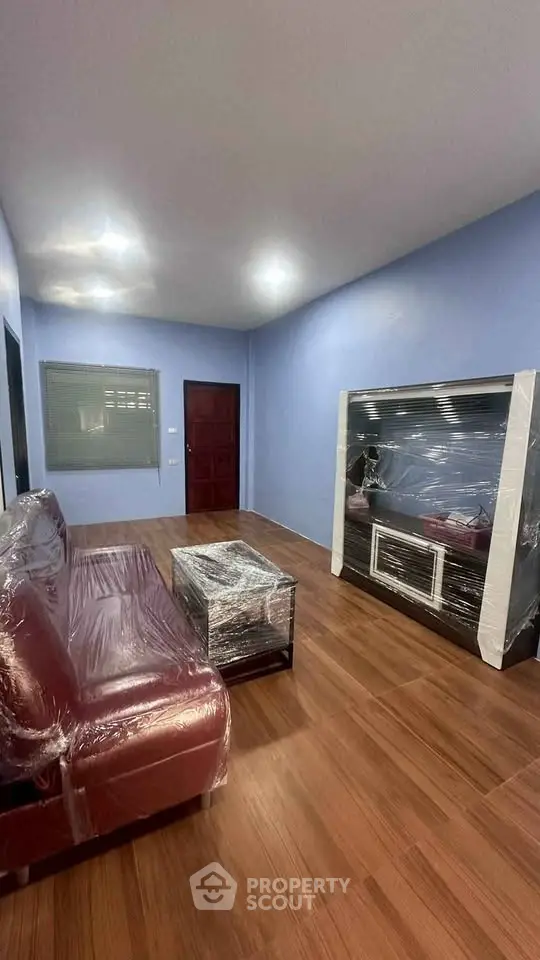 Spacious living room with new furniture wrapped in protective plastic, featuring modern design and wooden flooring.