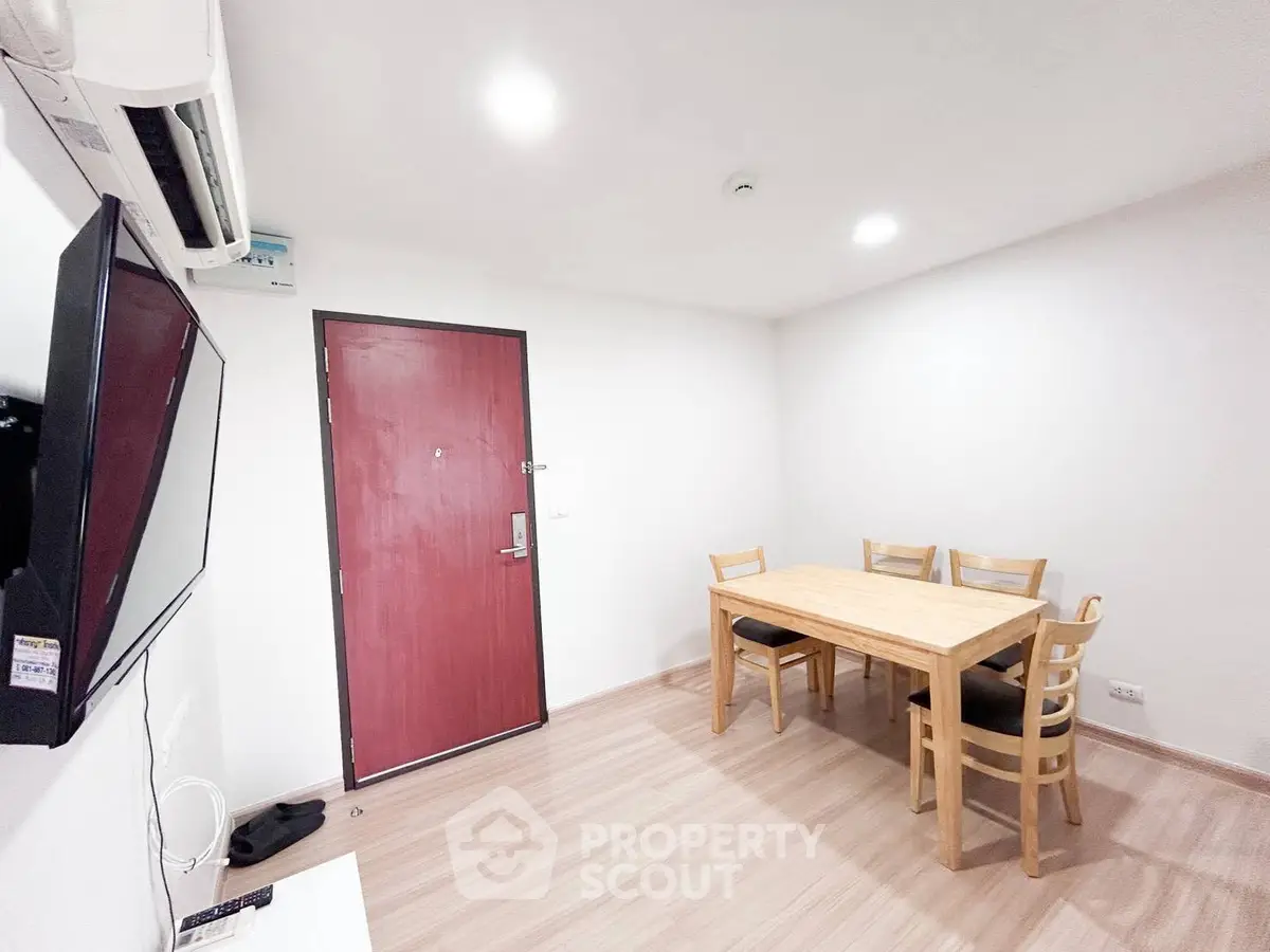 Modern dining area with wooden table and chairs, featuring a wall-mounted TV and air conditioning.