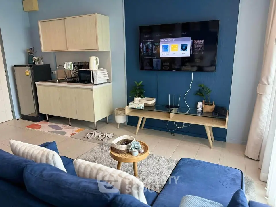 Modern living room with stylish furniture and entertainment setup, featuring a cozy blue sofa and sleek kitchenette.