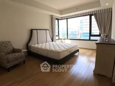 Spacious bedroom with large windows and hardwood floors in modern apartment.