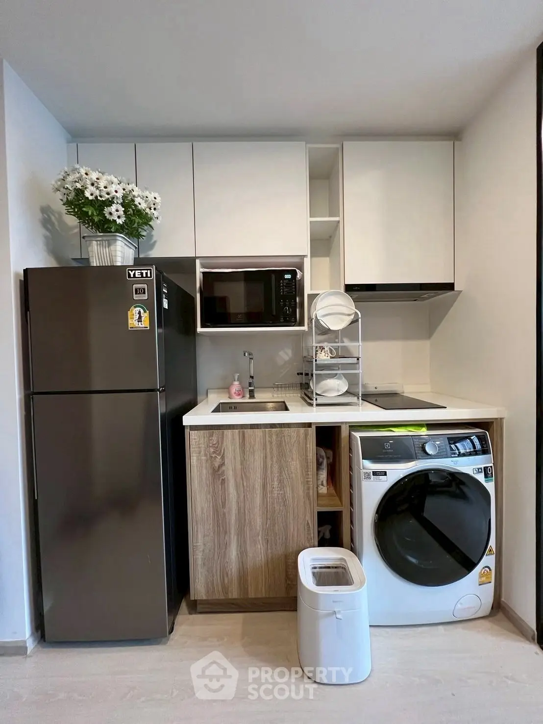 Modern compact kitchen with fridge, microwave, and washing machine in sleek design.
