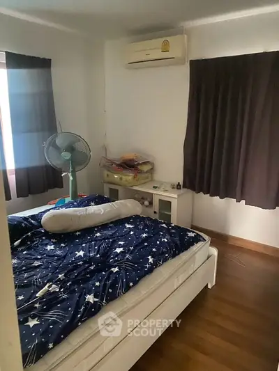 Cozy bedroom with air conditioning and wooden flooring, featuring a comfortable bed and dark curtains.